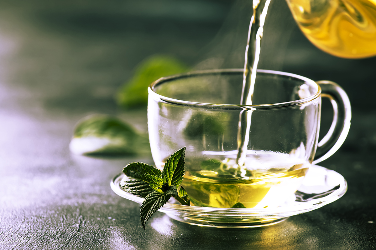 Hot chinese green tea with mint, with splash pouring from the ke